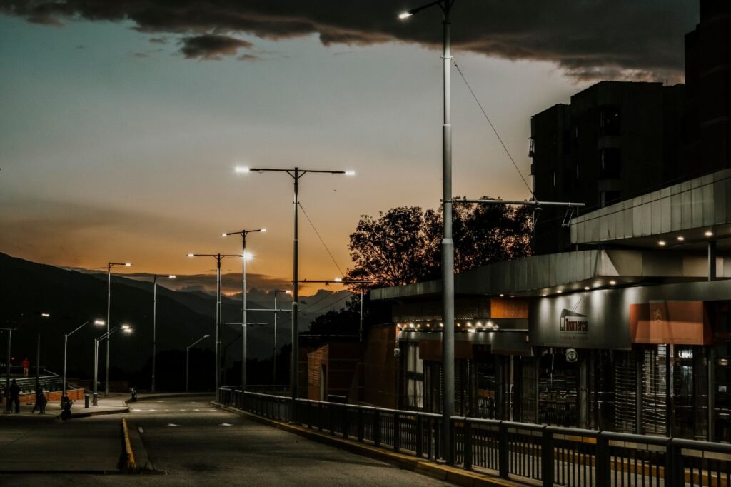 Solar-powered street lights in an urban plaza with pedestrians walking, captured at dusk.